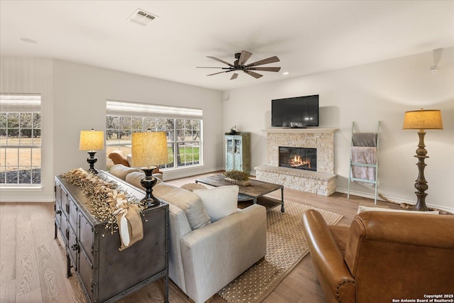 living room with a fireplace, visible vents, light wood-style flooring, a ceiling fan, and baseboards