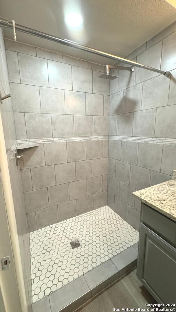 bathroom with vanity, wood-type flooring, a tile shower, and a textured ceiling