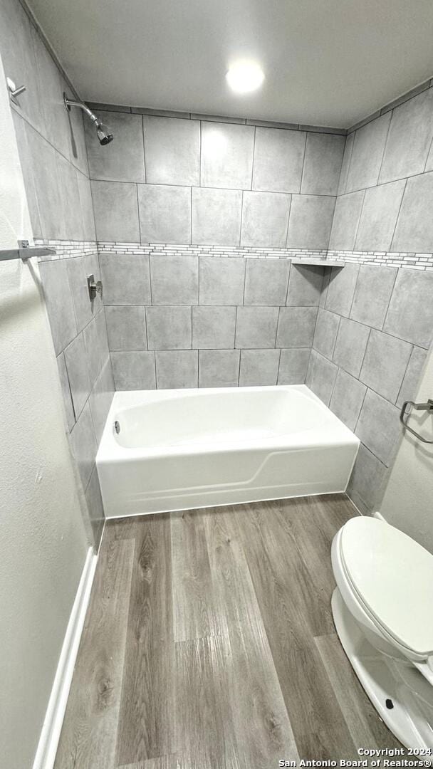 bathroom featuring hardwood / wood-style flooring, tiled shower / bath, and toilet