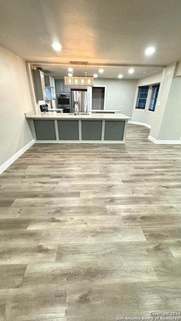 kitchen with hardwood / wood-style flooring, pendant lighting, stainless steel fridge, and kitchen peninsula