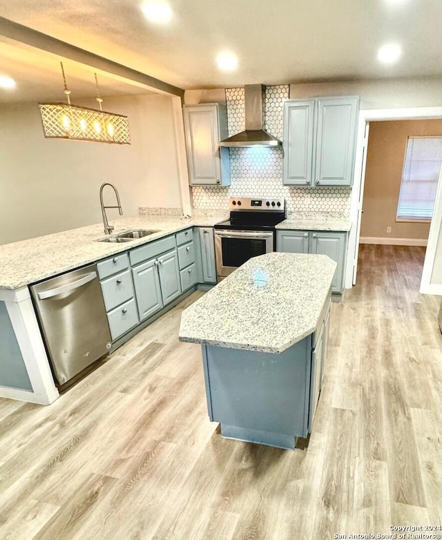 kitchen with appliances with stainless steel finishes, decorative light fixtures, sink, light hardwood / wood-style floors, and wall chimney range hood