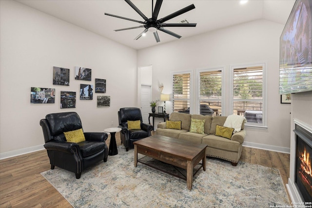 living room featuring a warm lit fireplace, baseboards, wood finished floors, and lofted ceiling