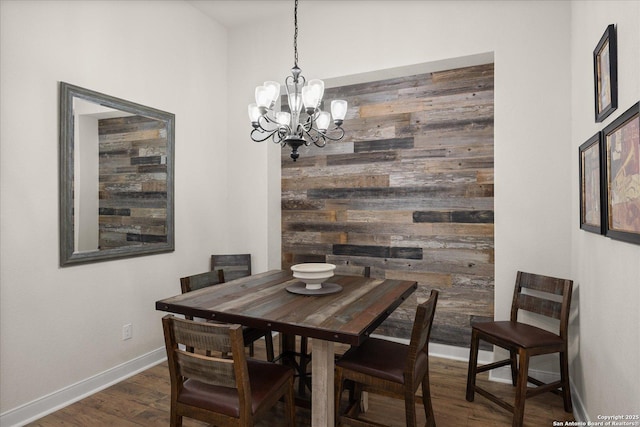 dining room with a chandelier, an accent wall, wood walls, wood finished floors, and baseboards