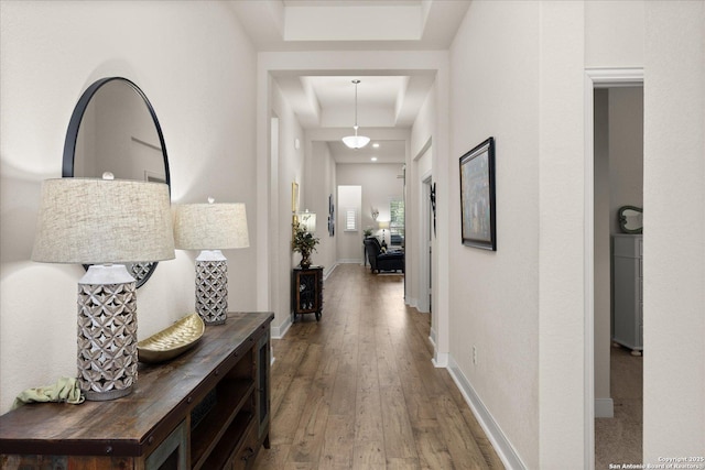 corridor featuring wood-type flooring, a raised ceiling, and baseboards