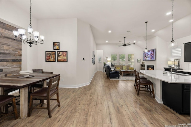 dining area featuring visible vents, a ceiling fan, lofted ceiling, a lit fireplace, and light wood-type flooring