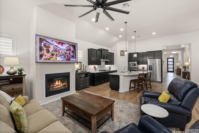 living room featuring recessed lighting, visible vents, light wood-style floors, a glass covered fireplace, and a ceiling fan