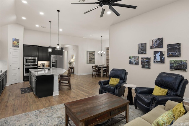 living room featuring recessed lighting, ceiling fan with notable chandelier, visible vents, baseboards, and light wood-style floors