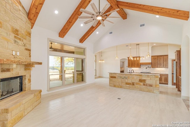 living room with beam ceiling, sink, a stone fireplace, and high vaulted ceiling