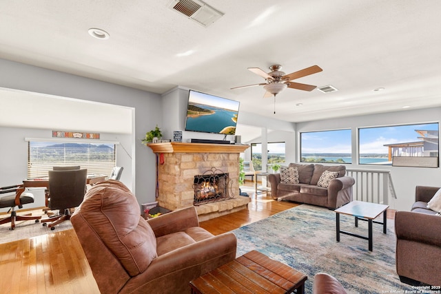 living room with ceiling fan, a stone fireplace, and light wood-type flooring