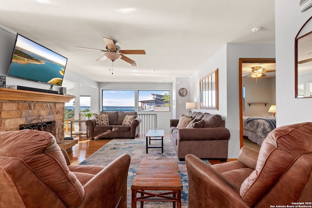 living room with hardwood / wood-style flooring, a stone fireplace, and ceiling fan