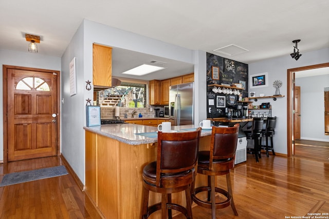 kitchen with dark hardwood / wood-style floors, stainless steel fridge, a kitchen bar, and kitchen peninsula