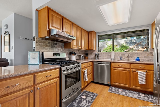 kitchen with appliances with stainless steel finishes, tasteful backsplash, sink, light stone countertops, and light hardwood / wood-style flooring