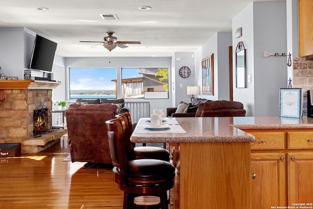 dining area featuring ceiling fan, a stone fireplace, and light hardwood / wood-style flooring