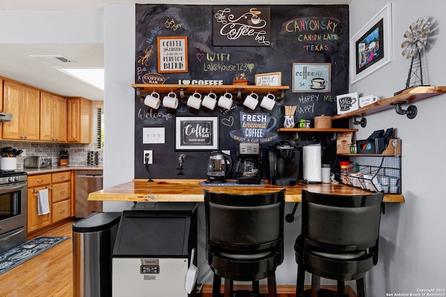 bar with tasteful backsplash, stainless steel appliances, butcher block countertops, and light wood-type flooring