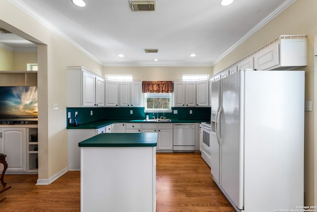 kitchen with sink, white appliances, crown molding, white cabinetry, and hardwood / wood-style floors