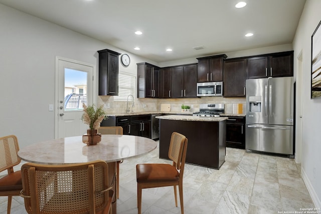 kitchen featuring sink, decorative backsplash, a center island, light stone counters, and stainless steel appliances