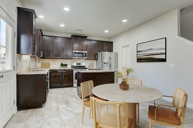 kitchen with sink, appliances with stainless steel finishes, dark brown cabinetry, light stone countertops, and a kitchen island