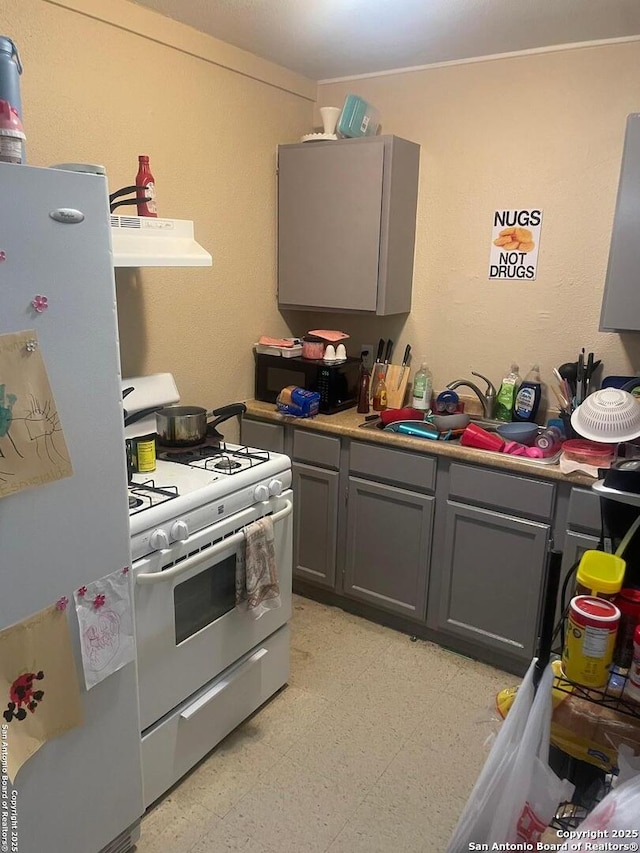 kitchen featuring gray cabinets, white gas range oven, and refrigerator