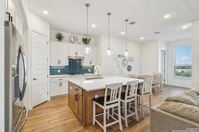 kitchen with appliances with stainless steel finishes, light wood-style flooring, visible vents, and under cabinet range hood