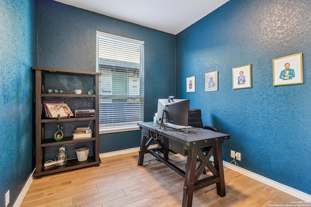 office area featuring a textured wall, baseboards, and wood finished floors