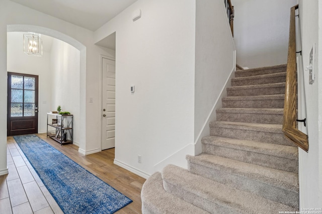 entrance foyer with arched walkways, stairway, baseboards, and wood finished floors