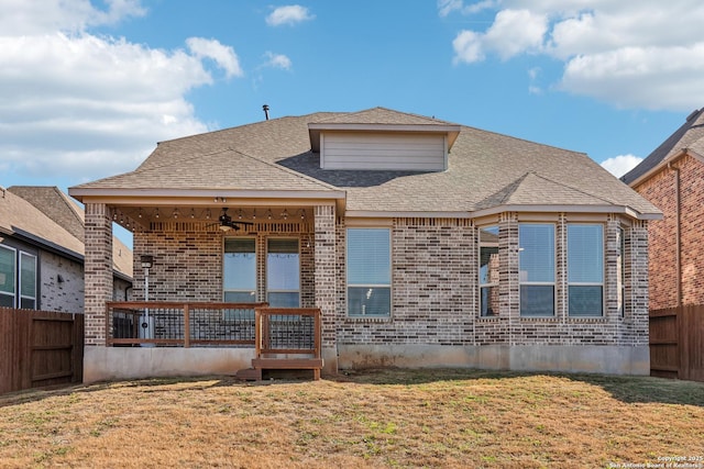 back of house featuring roof with shingles, a yard, brick siding, ceiling fan, and fence