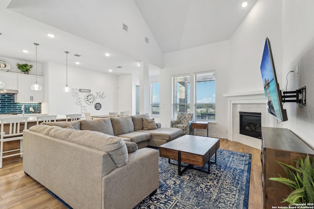 living area with a fireplace, recessed lighting, visible vents, light wood-style flooring, and high vaulted ceiling