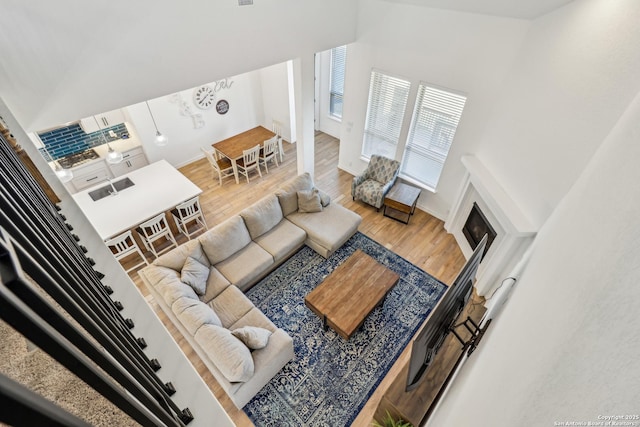 living area with high vaulted ceiling, a glass covered fireplace, wood finished floors, and baseboards