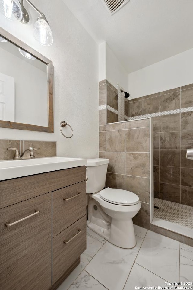 bathroom featuring vanity, toilet, and a tile shower