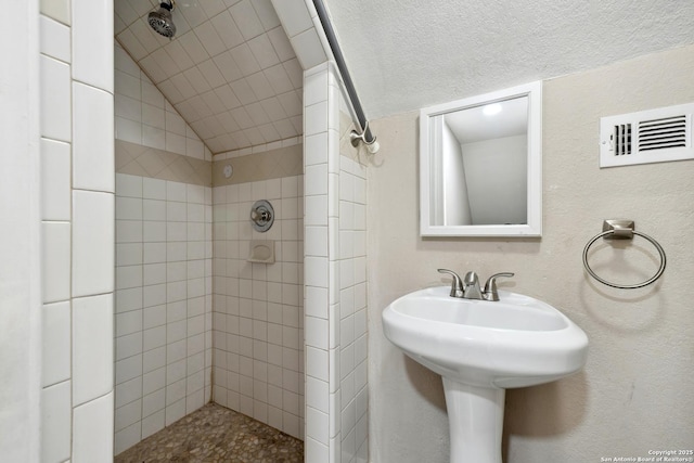 bathroom with lofted ceiling, tiled shower, and sink