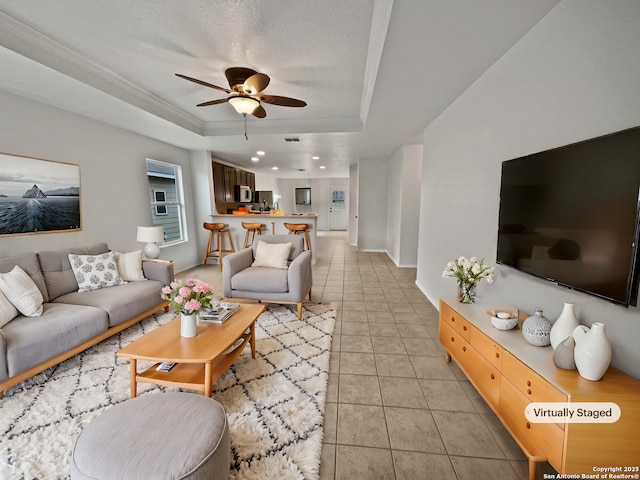 living room featuring ceiling fan, ornamental molding, a tray ceiling, and light tile patterned floors