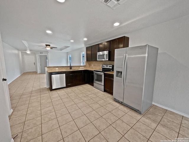 kitchen with sink, appliances with stainless steel finishes, backsplash, dark brown cabinets, and kitchen peninsula