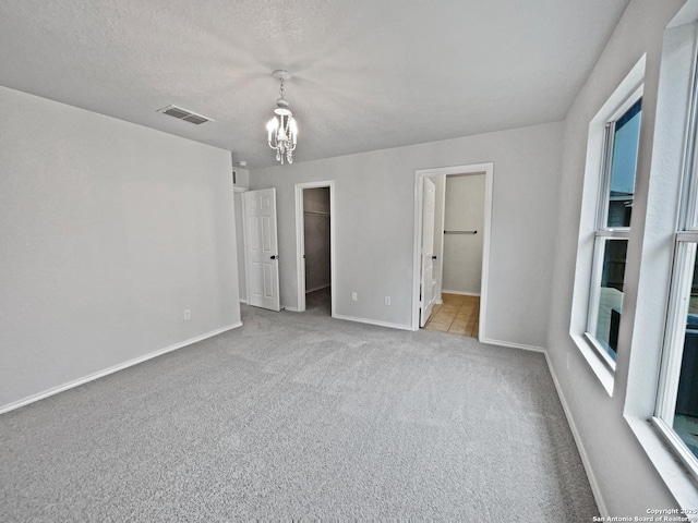 unfurnished bedroom featuring an inviting chandelier, connected bathroom, a textured ceiling, a walk in closet, and light colored carpet