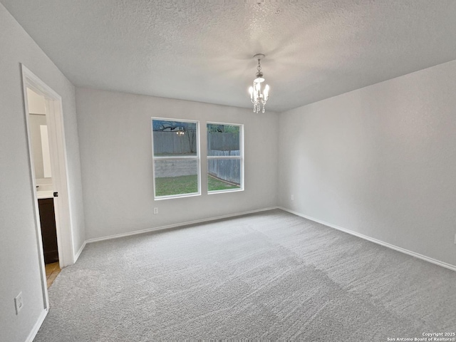 empty room featuring a notable chandelier, light colored carpet, and a textured ceiling