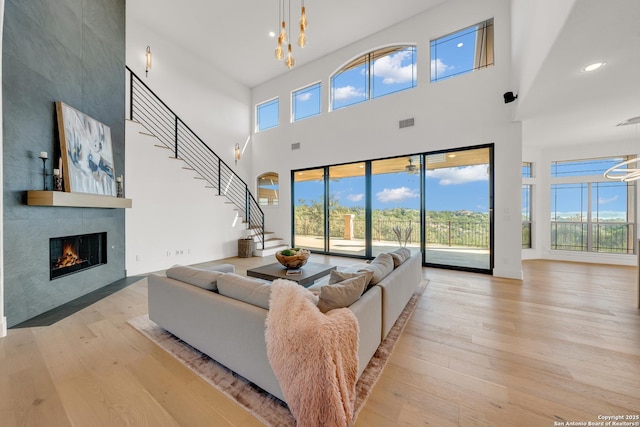 living area featuring a notable chandelier, a tile fireplace, stairway, and light wood-style floors
