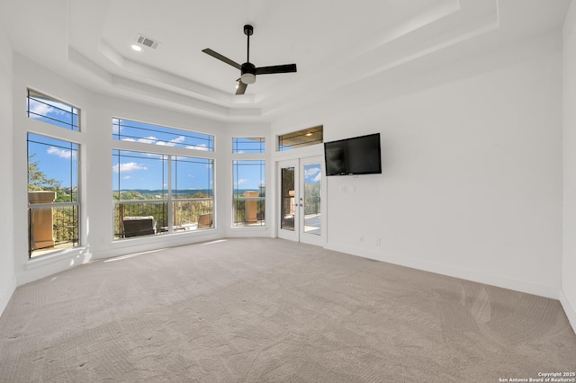 unfurnished living room featuring a high ceiling, a tray ceiling, ceiling fan, and carpet flooring