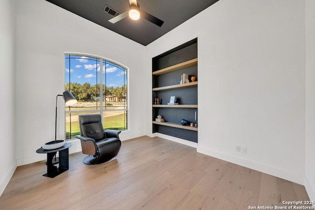 living area with built in shelves, ceiling fan, and light wood-type flooring