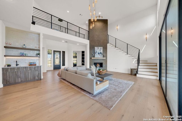 living room featuring a towering ceiling, indoor bar, a fireplace, and light wood-type flooring