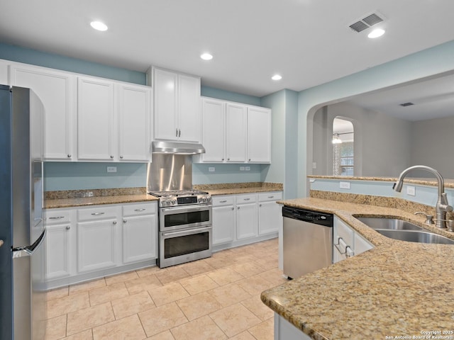 kitchen with sink, light tile patterned floors, appliances with stainless steel finishes, light stone countertops, and white cabinets