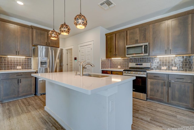 kitchen featuring sink, hanging light fixtures, light wood-type flooring, stainless steel appliances, and a kitchen island with sink