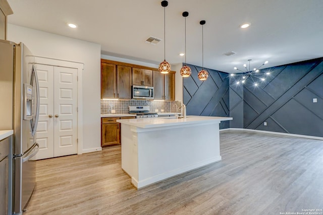 kitchen with decorative light fixtures, a center island with sink, light hardwood / wood-style floors, and appliances with stainless steel finishes