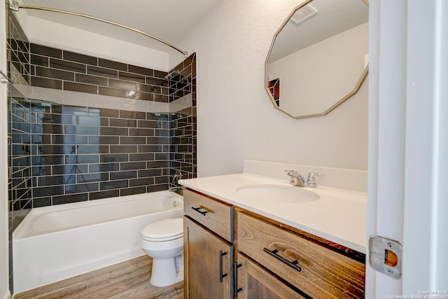 full bathroom with tiled shower / bath combo, vanity, hardwood / wood-style flooring, and toilet