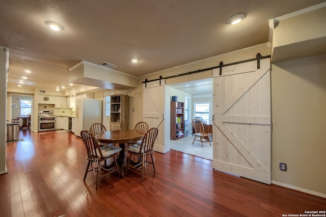 dining room with ornamental molding, a barn door, and hardwood / wood-style floors