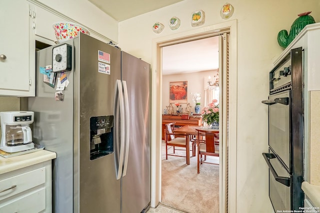 kitchen with stainless steel refrigerator with ice dispenser, white cabinetry, light colored carpet, and an inviting chandelier