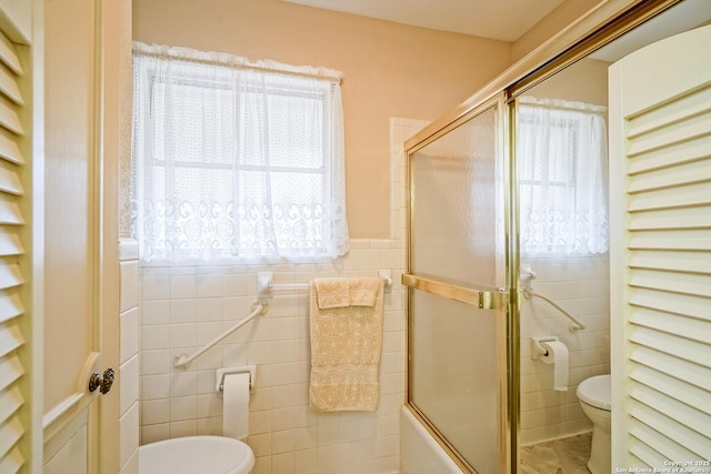 bathroom with tile walls, bath / shower combo with glass door, and toilet