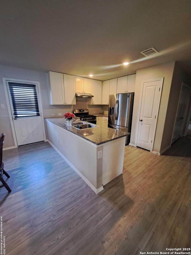 kitchen with white cabinets, dark stone counters, kitchen peninsula, stainless steel appliances, and light wood-type flooring