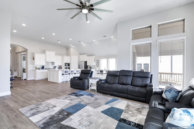 living room with a towering ceiling, light hardwood / wood-style floors, and ceiling fan