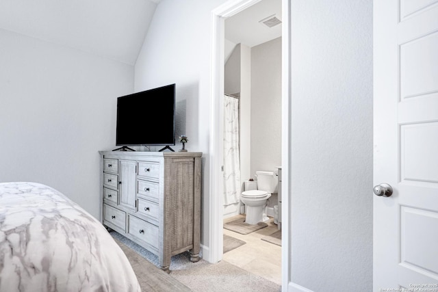 bedroom with connected bathroom, vaulted ceiling, and light carpet