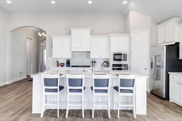 kitchen featuring lofted ceiling, appliances with stainless steel finishes, white cabinets, a kitchen island with sink, and backsplash