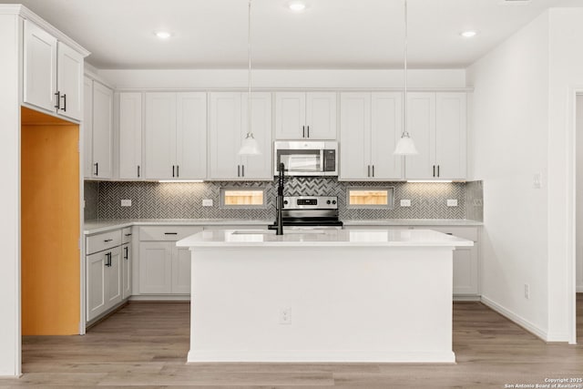 kitchen featuring white cabinetry, appliances with stainless steel finishes, an island with sink, and decorative light fixtures